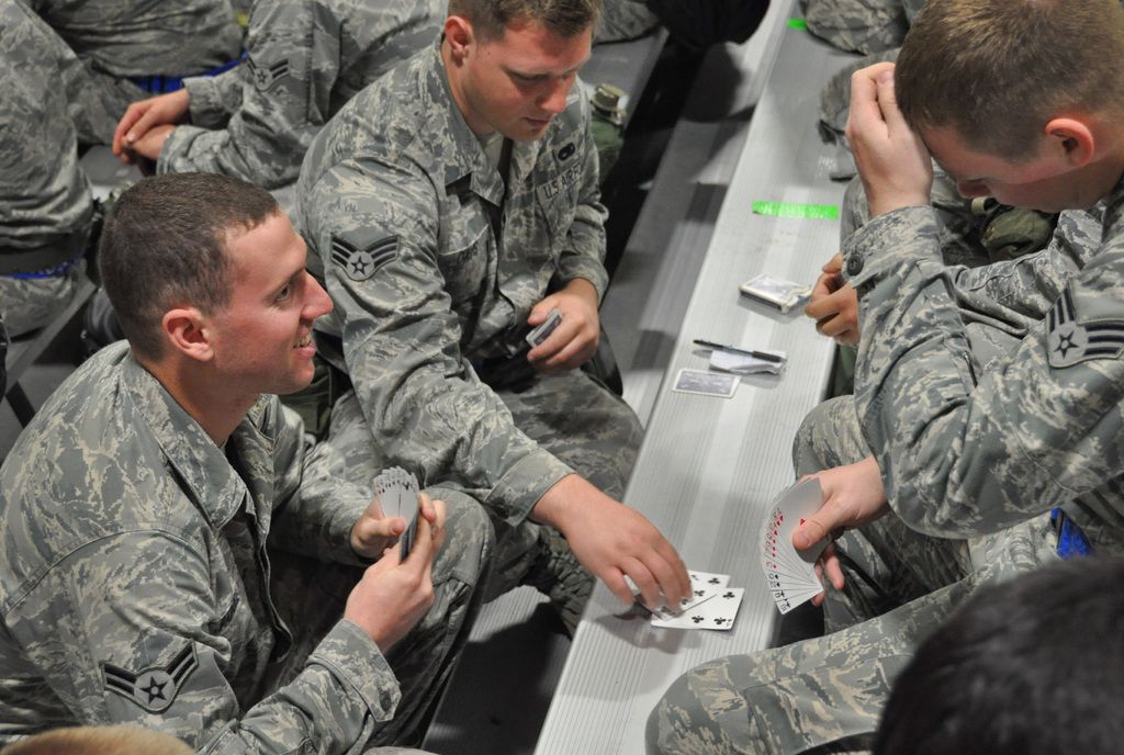 In this image there are people sitting on benches and playing cards.